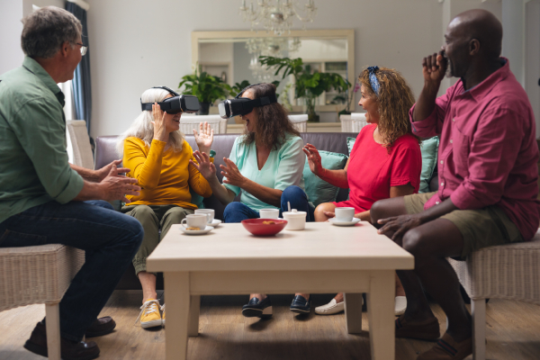 Happy multiracial senior woman and men with friends using vr headsets in living room at home. unaltered, lifestyle, social gathering, friendship, virtual reality, futuristic and modern technology.